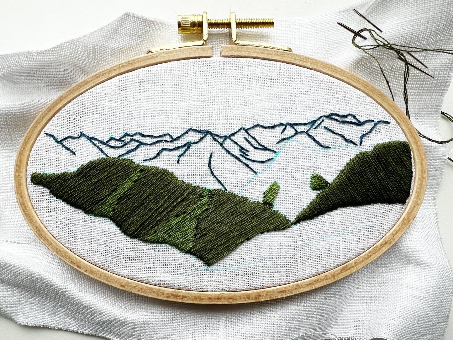 Embroidery hoop with mountain landscape design on white fabric