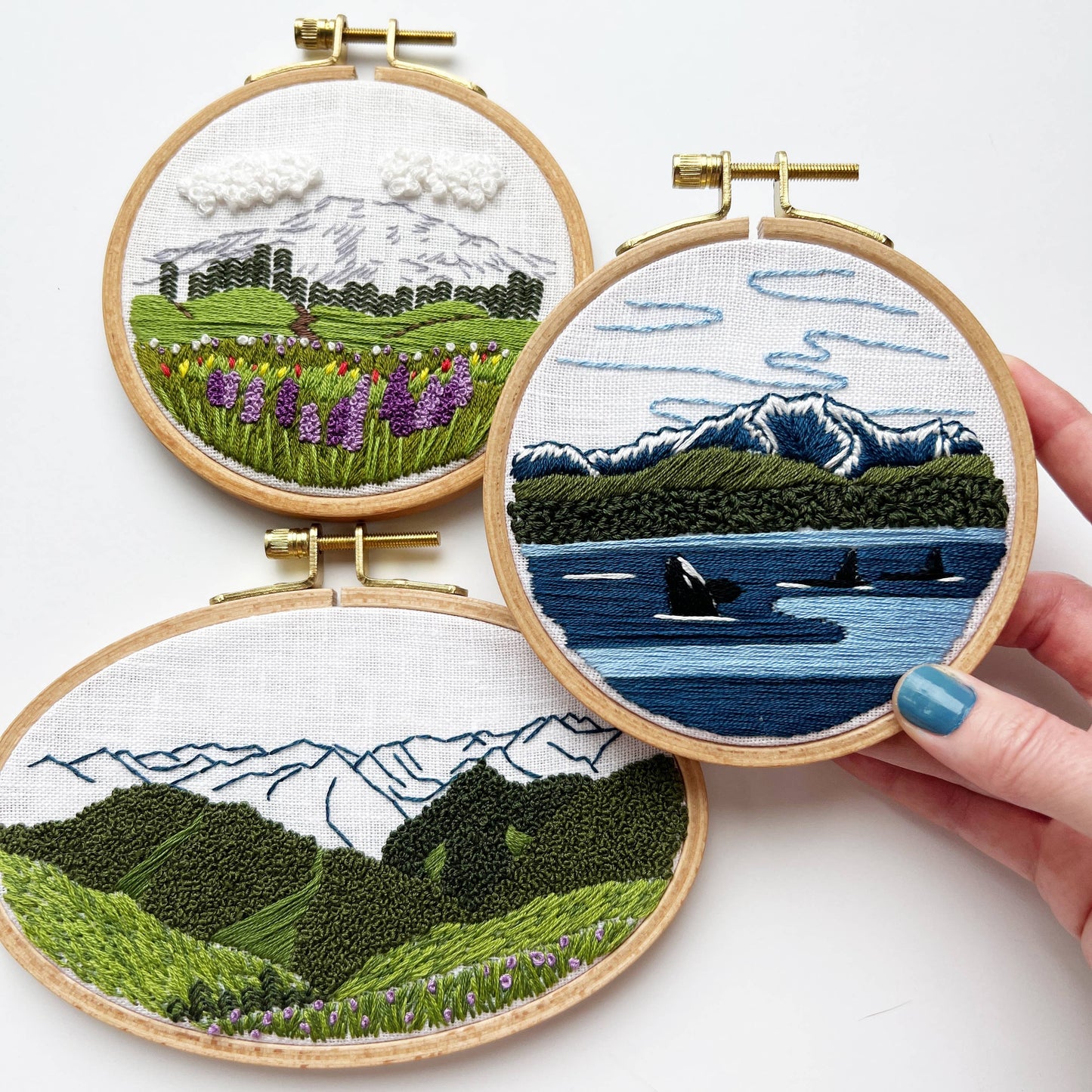 Three embroidery hoops with mountain and landscape designs on a white background.