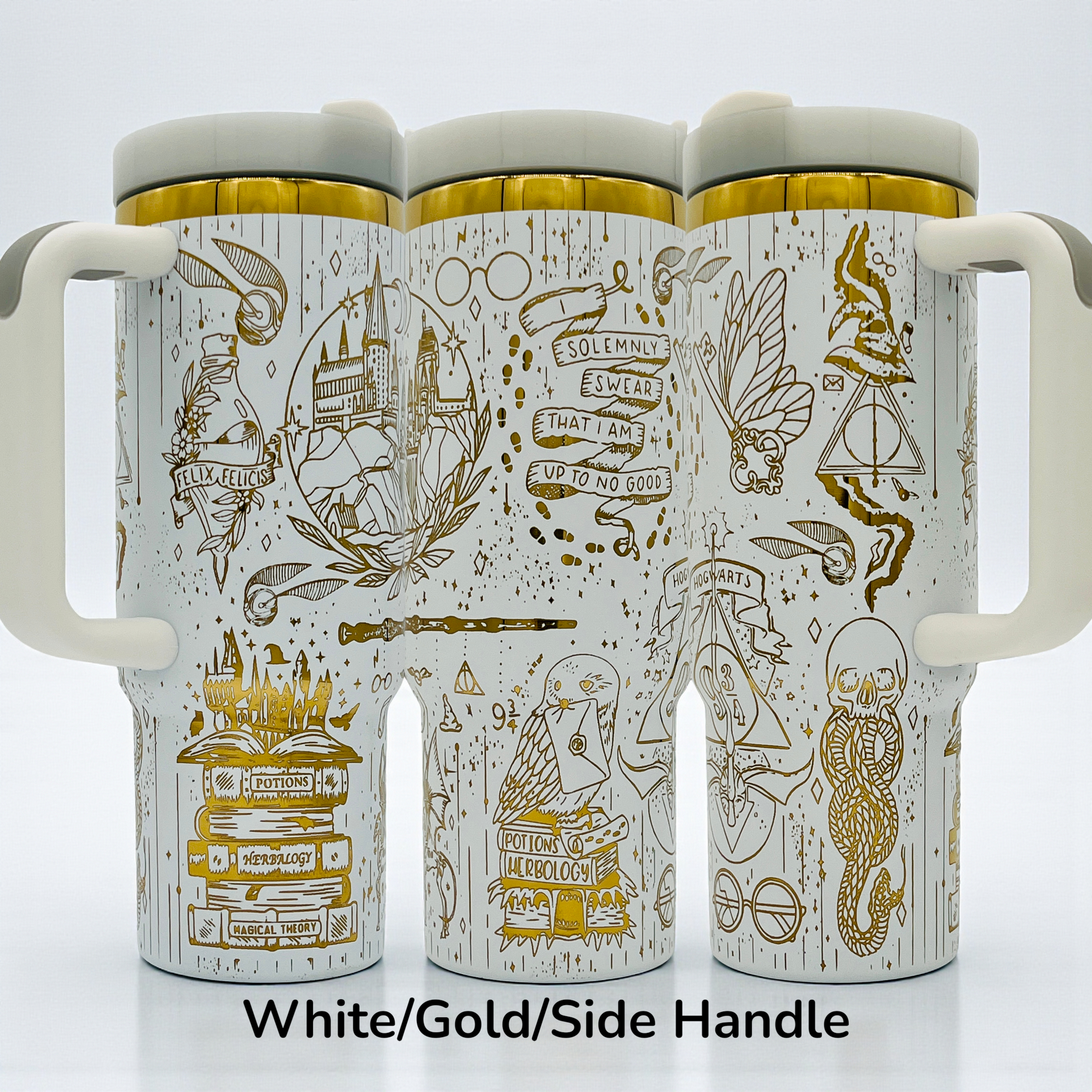 White mugs with gold magical designs, including castles, scrolls, and symbols, with side handles.