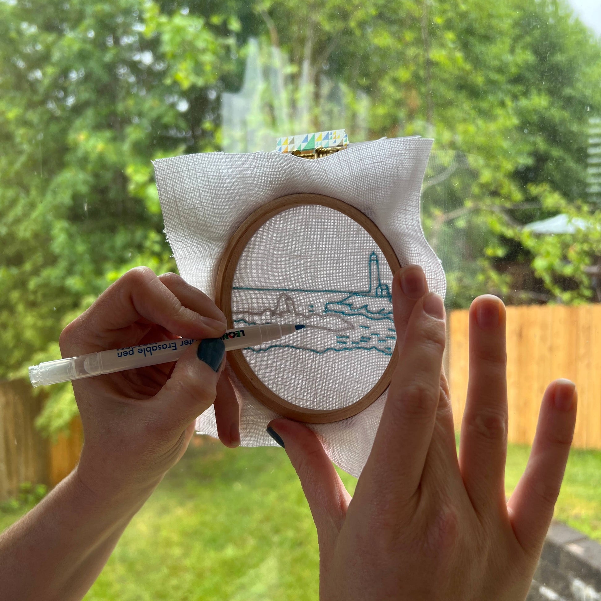 Person holding an embroidery hoop with a partially completed design outdoors.