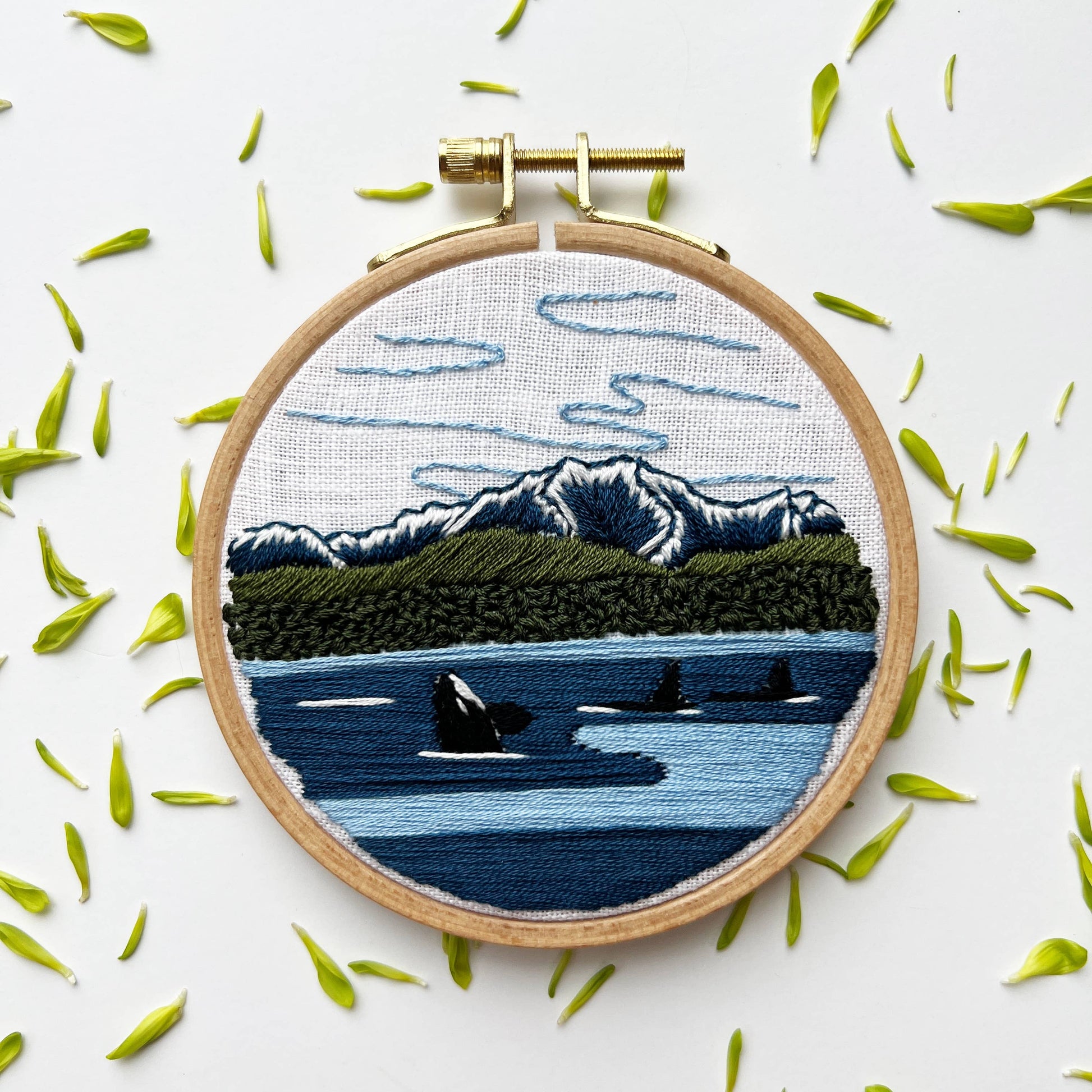 Embroidery hoop with a scenic landscape design featuring mountains, water, and boats on a white background.