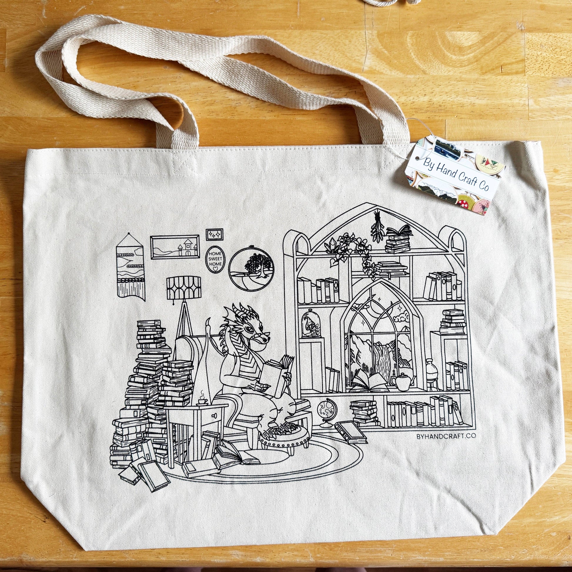 Tote bag with black and white illustration of a cat in a library on a wooden surface