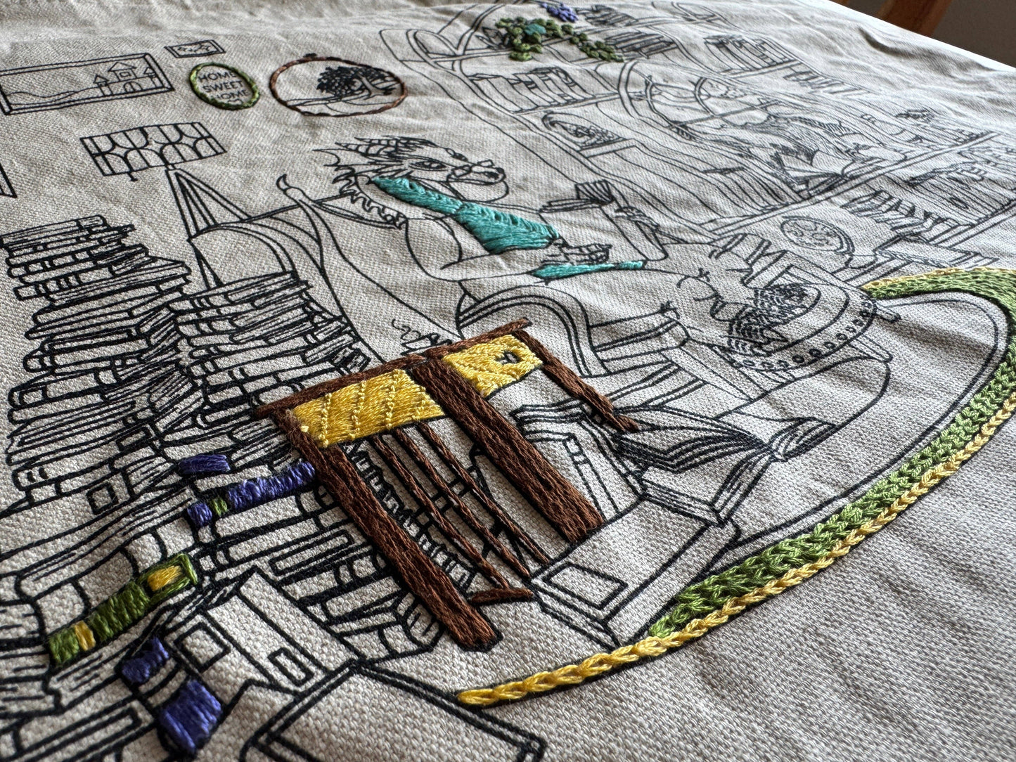 Embroidery of a detailed scene with books, a chair, and other elements on fabric.