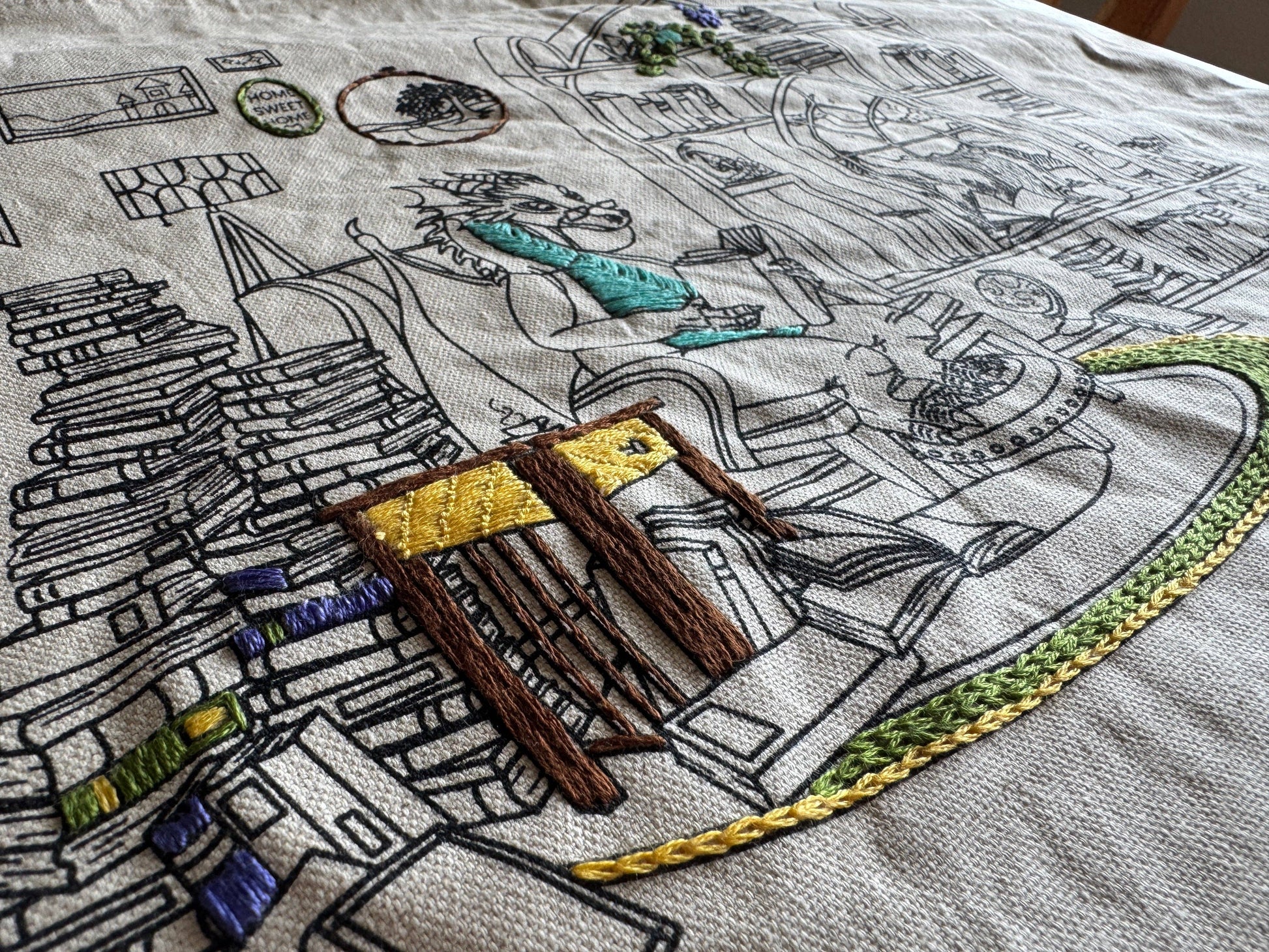 Embroidery of a detailed scene with books, a chair, and other elements on fabric.