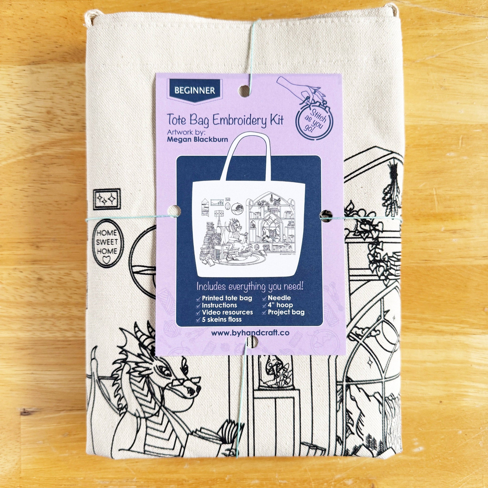 Tote bag embroidery kit packaging on a white tote bag with black line art design on a wooden surface