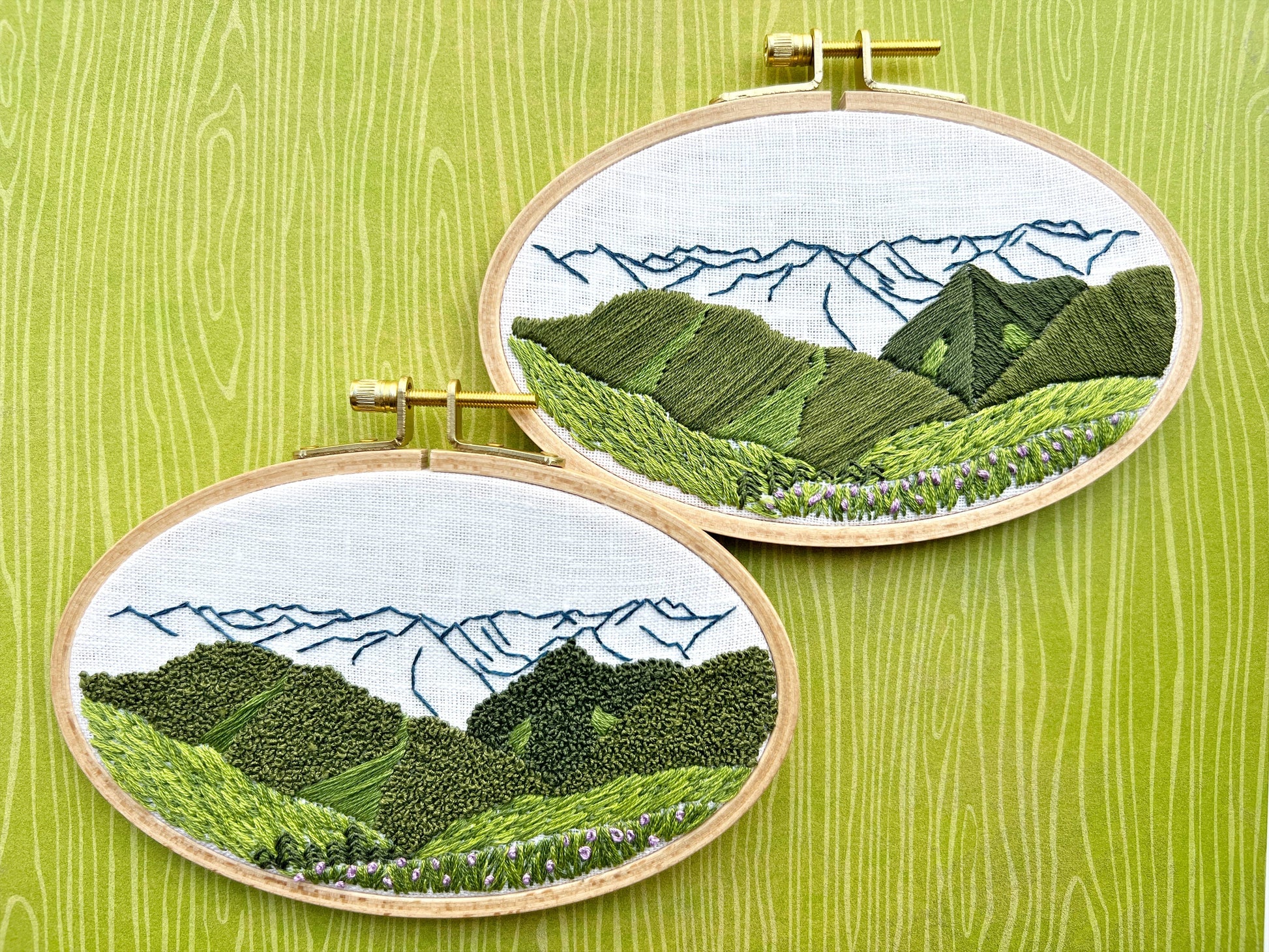 Two embroidered landscapes in wooden hoops on a green wooden background