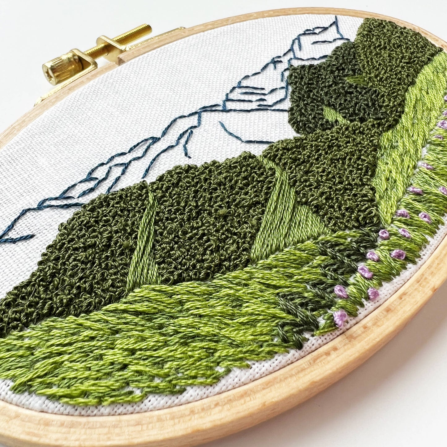 Embroidery hoop with green landscape design on a white background
