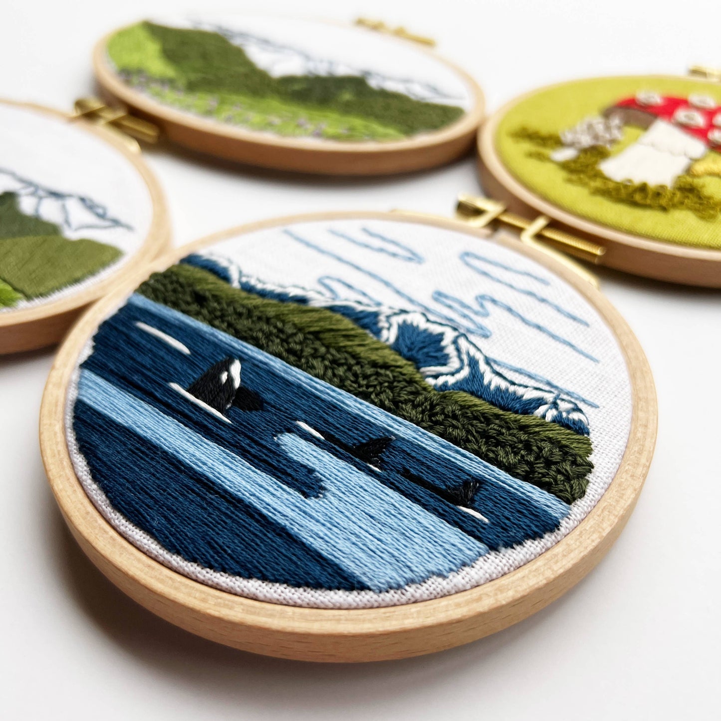 Embroidery hoops with mountain and landscape designs on a white background