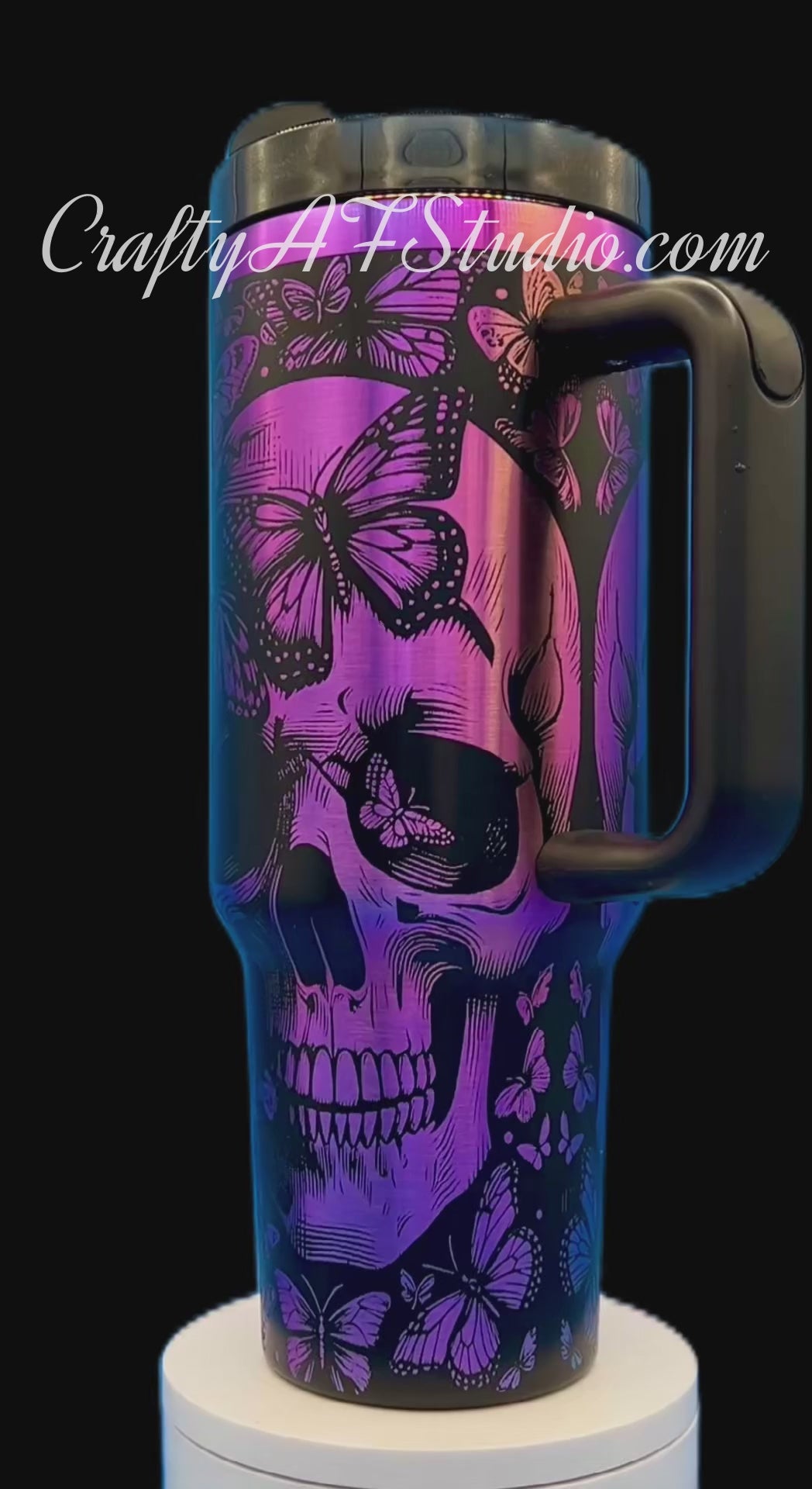 Purple travel mug with black skull and butterfly design, black handle and lid, on a white stand.