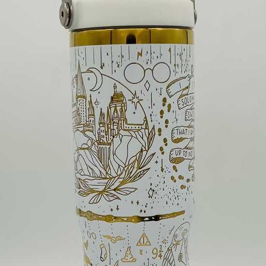 White tumbler with gold illustrations of a castle, glasses, footprints, and magical symbols.