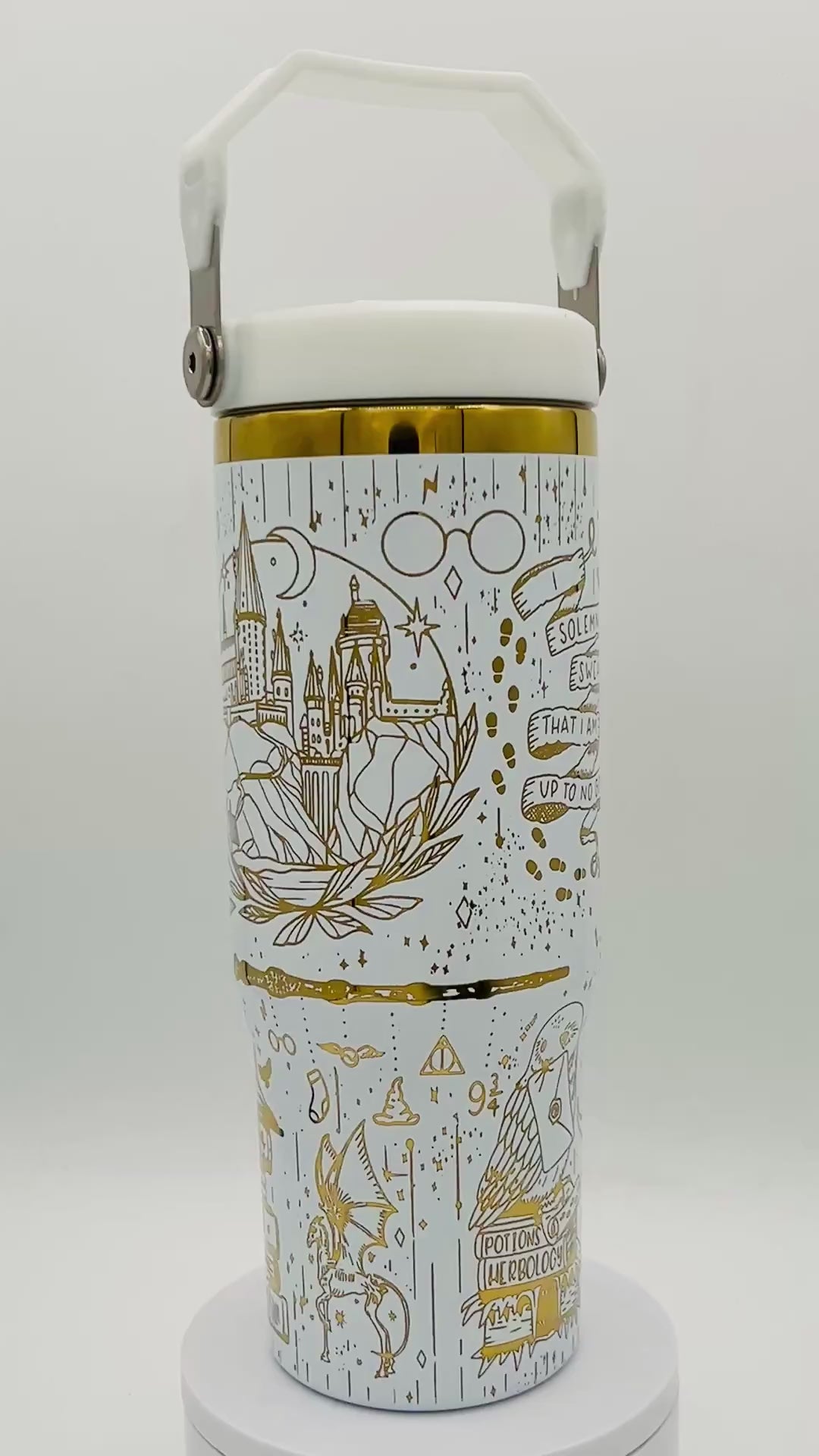 White tumbler with gold illustrations of a castle, glasses, footprints, and magical symbols.